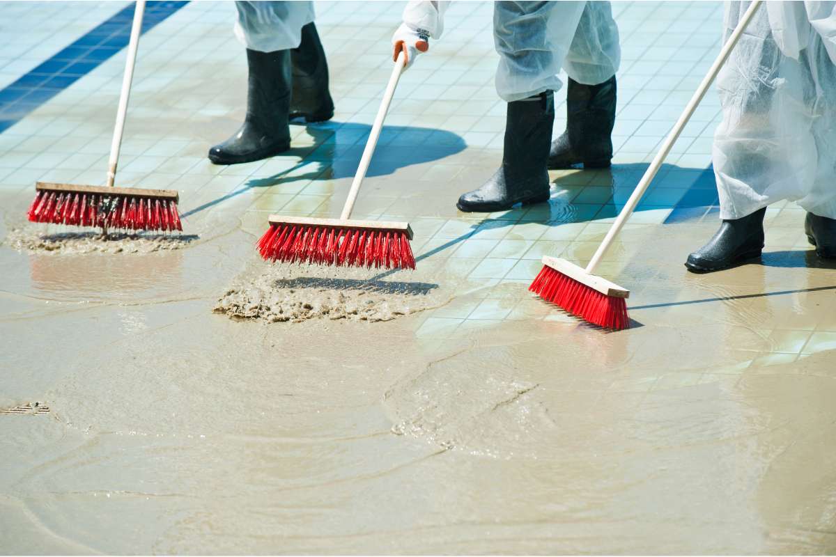 nettoyage-apres-inondation Des personnes utilisent des raclettes et des brosses pour nettoyer le sol après les inondations